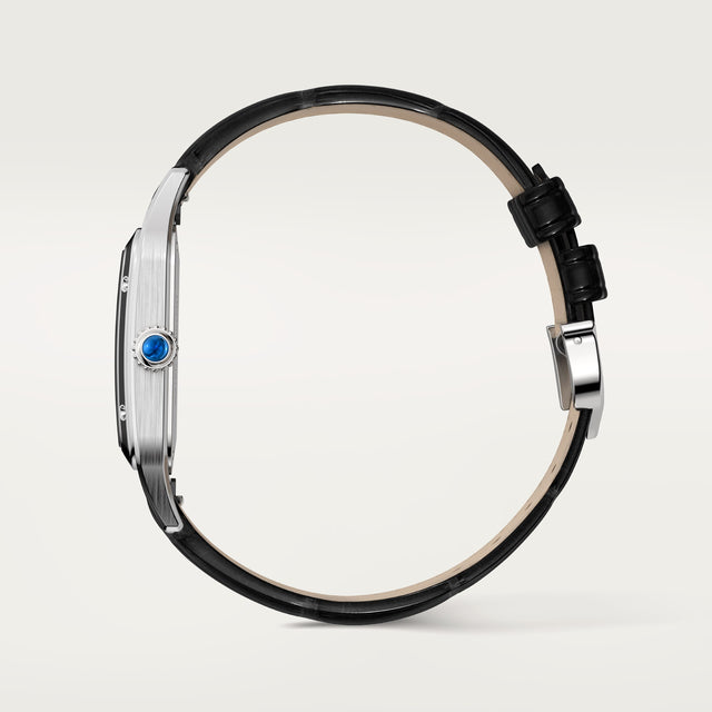 A side view of the Cartier Santos-Dumont watch featuring a thin steel case, black leather strap, and a blue gemstone in the crown, set against a light background.