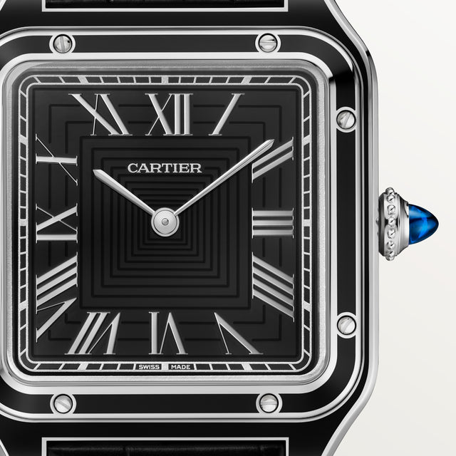 Close-up of the Cartier Santos-Dumont watch, featuring a black and silver geometric square dial with Roman numerals, silver hands, a steel case with blue cabochon crown, and a black leather strap.